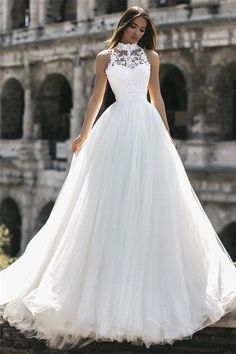 a woman in a white wedding dress standing on a stone wall with an old building in the background