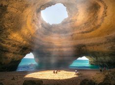 people are sitting on the beach in front of an arch shaped rock formation with sunlight streaming through it