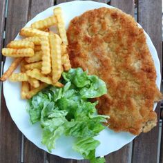 a white plate topped with fried chicken and french fries next to lettuce on top of a wooden table