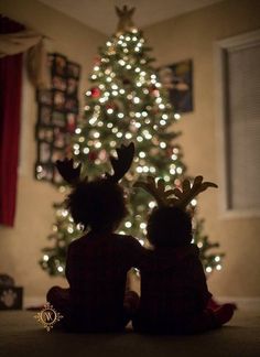 two children sitting in front of a christmas tree