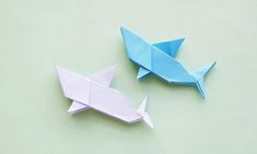 two origami fish on a green surface one is blue and the other is white