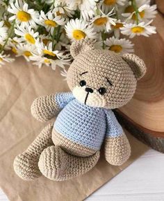 a crocheted teddy bear sitting on top of a piece of paper with daisies in the background