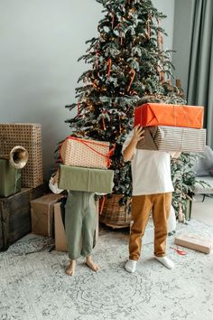 a young boy holding presents in front of a christmas tree