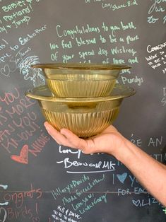 a person holding a bowl in front of a chalkboard wall with writing on it