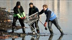 three people with a shopping cart in the water on a beach, one pushing it