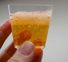 a hand is holding a small glass with liquid in it and bubbles on the bottom