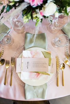 the table is set with silverware and pink flowers