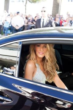 a woman sitting in the driver's seat of a car with people standing around