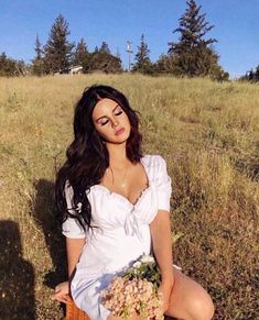 a woman sitting in the grass with her eyes closed and holding a basket full of flowers