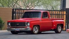 an old red pickup truck parked in front of a gate