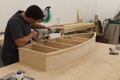 a man working on a wooden boat in a woodworking shop with tools and supplies