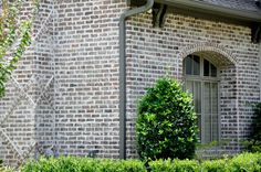 a brick building with a clock on it's side and bushes around the corner