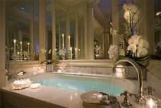 a bathtub with candles and flowers on the side in a room filled with windows