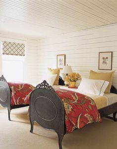 two beds in a room with white walls and carpeted flooring, one has a red blanket on it