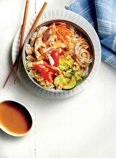 a bowl of noodles and vegetables with chopsticks next to it on a plate