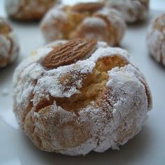 powdered sugar covered donuts with almonds on top are sitting on a white plate