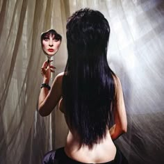 a woman with long black hair is looking at herself in the mirror