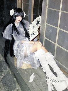 a woman with long black hair and white boots sitting on a bench in front of a window