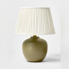 a green lamp with a white shade on it's base and a beige lampshade