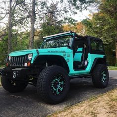 a blue jeep is parked on the side of the road in front of some trees