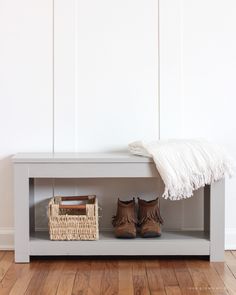 a white bench with some shoes and a basket on it next to a wooden floor