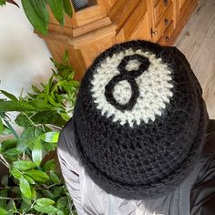 a crocheted hat with the number six on it sitting next to a plant