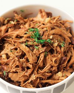 a white bowl filled with shredded meat and garnish