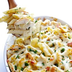 a wooden spoon scooping some pasta from a casserole dish with chicken and cheese