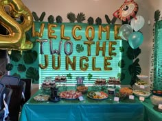 a welcome to the jungle themed party with balloons and desserts on a blue table