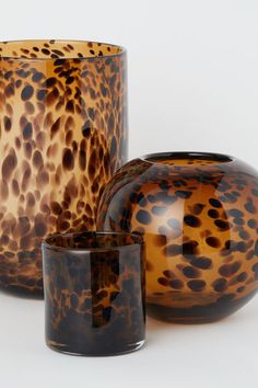 three glass vases sitting next to each other on a white surface with brown spots