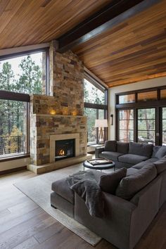 a living room with large windows and a stone fireplace in the center, surrounded by wood flooring