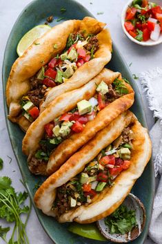 three tacos with meat, vegetables and sauce on a plate next to a bowl of salsa