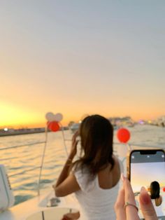 a woman taking a photo on her cell phone while sitting in a boat at sunset