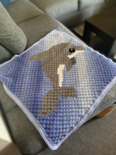 a crocheted square with a bird on it sitting on a couch in the living room