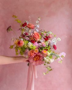 a woman holding a bouquet of flowers in her hand against a pink wall with the background