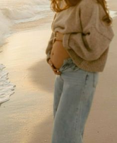 a woman standing on top of a beach next to the ocean with her stomach exposed