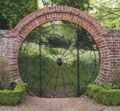 an iron gate in the middle of a brick wall surrounded by bushes and trees,