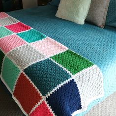 a crocheted blanket on top of a bed with two pillows in the background