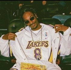 a man sitting in a chair with his hands on his hips wearing sunglasses and a lakers jersey