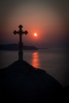 a cross on top of a hill with the sun setting in the distance behind it