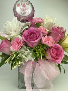 a bouquet of pink roses and white flowers in a square vase with a baby girl balloon