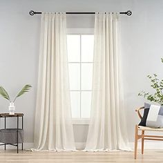 a living room with white curtains and a chair in front of the window, next to a potted plant