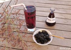 a bowl of blackberries next to a bottle of cold cola on a wooden table