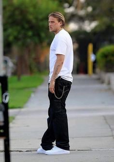 a man in white shirt and black pants standing on sidewalk next to parking meter with handbag