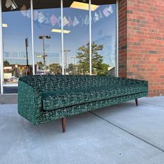 a green couch sitting on top of a sidewalk next to a building with glass windows