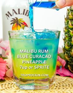 a person pouring blue curacao into a glass next to a pineapple drink