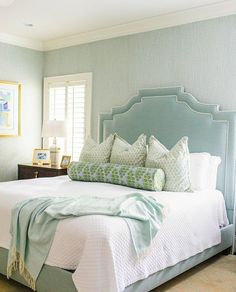 a bedroom with blue walls, white bedding and green pillows on the headboard