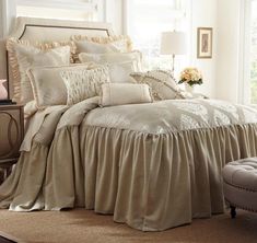 the bed is made up with ruffled sheets and pillows, along with a footstool