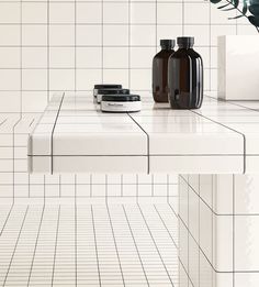 two bottles on top of a white counter in a room with tiled walls and flooring