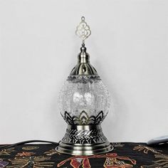 an ornate glass and metal table lamp on a black fabric covered table cloth with a white wall in the background